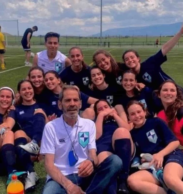 A group of people, probably a soccer team with their coach, posing joyfully on a soccer field