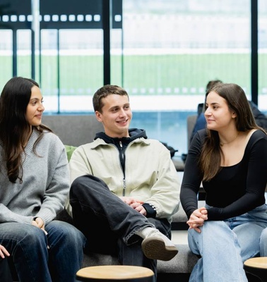 A group of young adults engaging in conversation in a modern lounge setting.