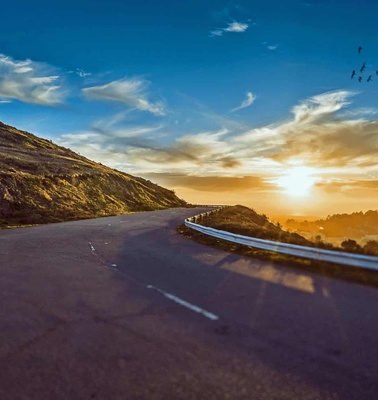 A scenic view of a winding road at sunset with hills and a flock of birds flying in the sky.