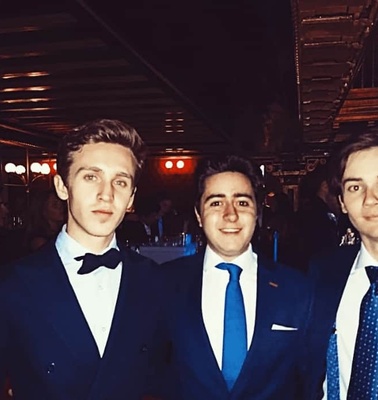 Three young men in formal attire smiling at a social event.