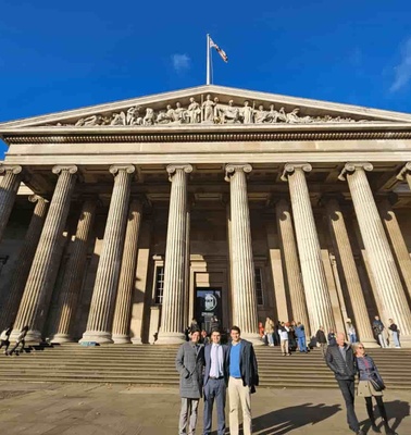 People standing in front of the British Museum, which features a classical facade with tall columns under a clear blue sky.