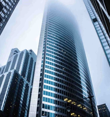 A view looking up at towering skyscrapers with a foggy sky above.