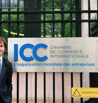A young man in a suit standing in front of the International Chamber of Commerce entrance.