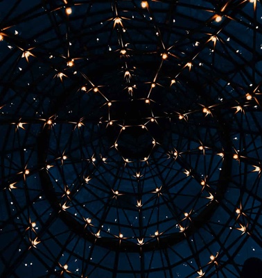 A view from below of a dome structure illuminated by small hanging lights against a twilight sky.