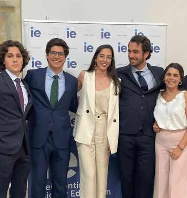 A group of six people, three men and three women, dressed in business attire, smiling and posing together at an IE event.