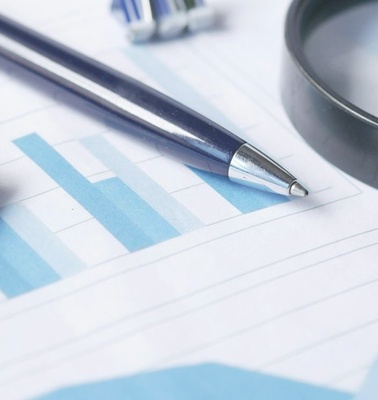 An assortment of office tools including a calculator, a pen, and a magnifying glass on a financial report.