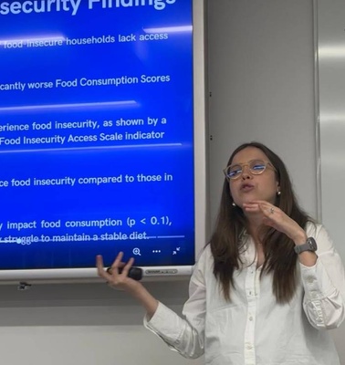 A woman is presenting on food insecurity in front of a projection screen displaying research findings.