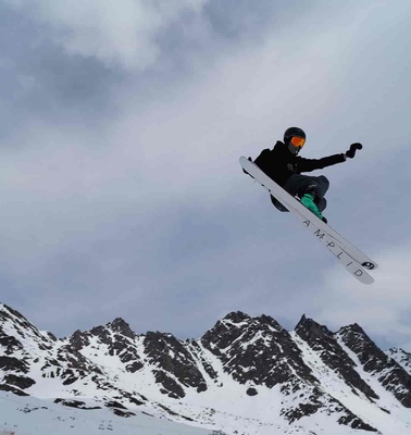 A skier performing a jump against a backdrop of snowy mountains.