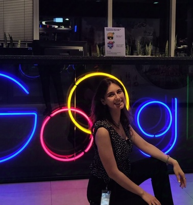 A woman smiling while sitting in front of a colorful neon Google sign at night.