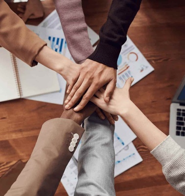 A group of people stacking hands over a wooden table in a teamwork gesture.