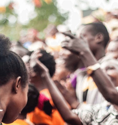 A crowd of people cheering and celebrating at an outdoor event, focusing on a woman in the foreground who is smiling.