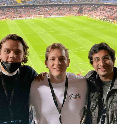 Three young men smiling at the camera in a crowded stadium during a sports event.