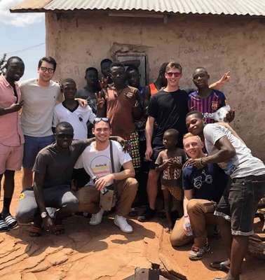 Group of diverse people smiling and posing together in front of a rustic building with a pile of logs nearby