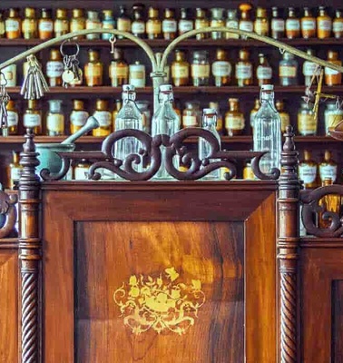 An old-fashioned pharmacy interior with wooden counters and numerous small drawers filled with bottles.