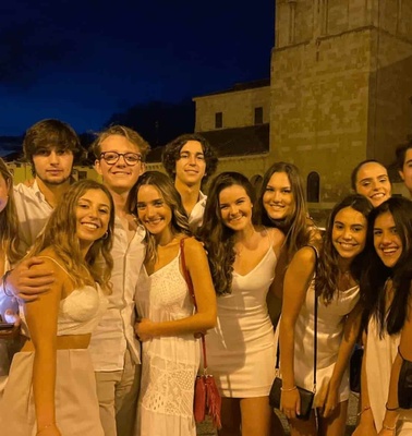 A group of young adults smiling and posing together at night in front of a historical building.