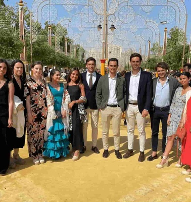 A group of people dressed in formal and semi-formal attire posing for a photo at an outdoor event with decorative structures in the background.