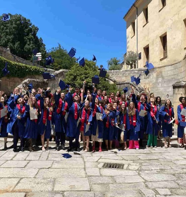 A group of graduates celebrating outdoors, tossing their blue caps in the air, in front of a historic building.