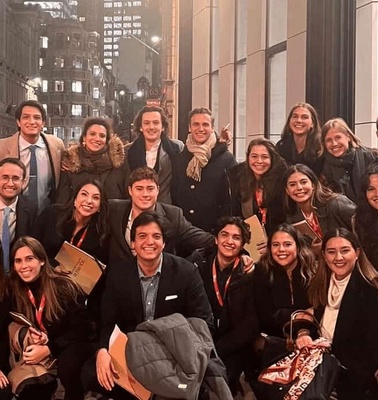 A group of young adults dressed in business attire smiling in a city setting.