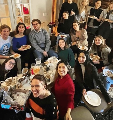 A group of people of various ethnicities smiling and holding plates of food at a social gathering inside a room.