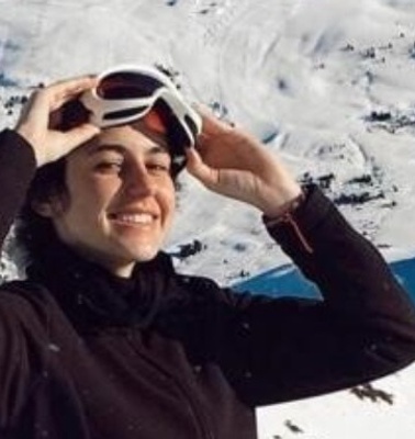 A person with a cheerful expression adjusts ski goggles on a snowy mountain landscape.