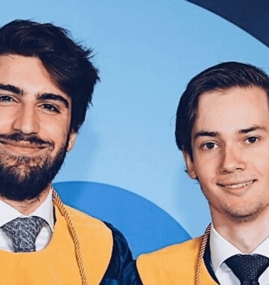 Two young men in graduation attire standing proudly at IE University.