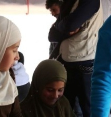 A UNICEF worker in a blue vest interacts with people inside a tent.