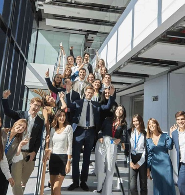 A group of professionally dressed individuals celebrating outside a modern office building.