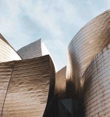 Modern architecture with curved stone walls and unique geometric shapes under a clear sky.