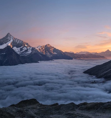 A breathtaking view of snow-capped mountains above a sea of clouds during sunrise.