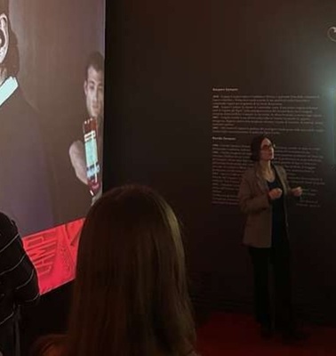 A woman is giving a presentation in front of a large screen displaying portraits and historical information.