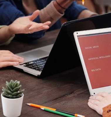 A group of people discussing ideas while using laptops on a wooden table.