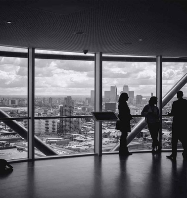 Silhouettes of four people standing in front of large windows overlooking a cityscape from a high vantage point.