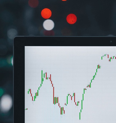 A laptop screen displaying a stock market chart, with a blurred background featuring bokeh lights.
