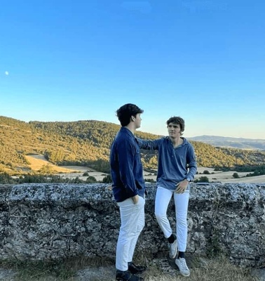 Two men chatting on a stone wall overlooking a scenic landscape during sunset.