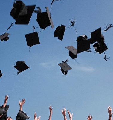 Graduation caps being tossed into the air under a clear blue sky