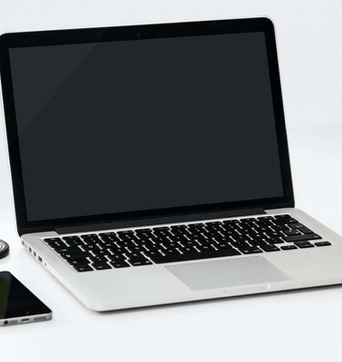 A modern workspace setup with an open laptop, a smartphone, a wristwatch, and a red apple on a white surface.
