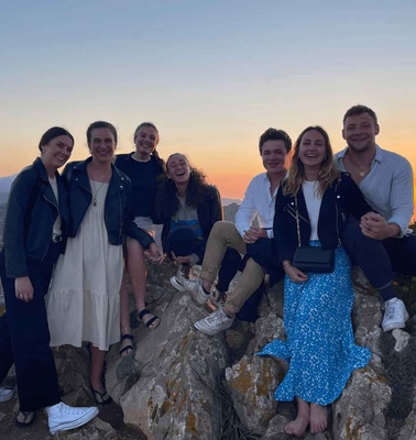 A group of people sitting on rocks enjoying a sunset in the background