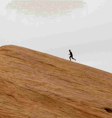 A person running on a large smooth sandstone hill under a cloudy sky.