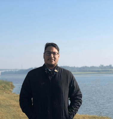 A man standing in front of a tranquil river under a clear sky during the day.