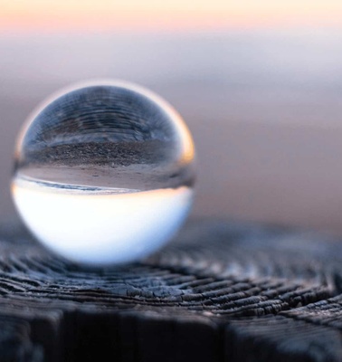 A crystal ball sitting on a weathered wooden surface, reflecting the sunset on a beach.