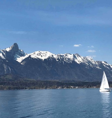 A sailboat on a calm lake with snow-capped mountains in the background under a clear blue sky.