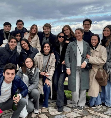 A group of people posing for a photo on a beachfront with cloudy skies and the ocean in the background.
