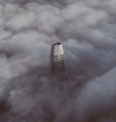 A skyscraper emerges from a dense blanket of clouds.