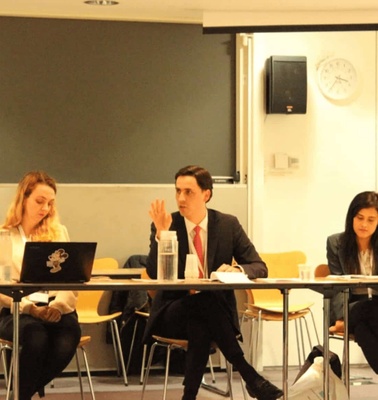 A group of professionals are seated around a table in a meeting room, discussing actively.