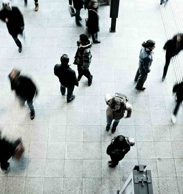 A high angle view of a busy pedestrian area with people walking in different directions, some blurred due to motion.