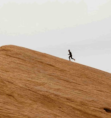 A person running on a large, sloping sand dune under a cloudy sky.