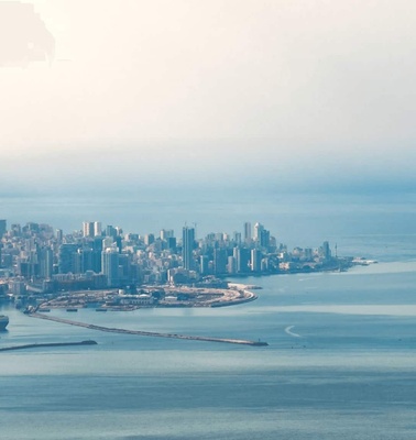 Aerial view of a coastal city skyline with high-rise buildings and a body of water under a hazy sky