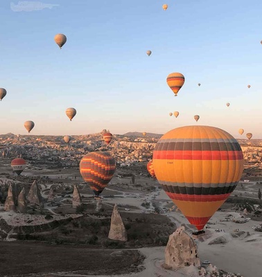 Colorful hot air balloons floating above a rocky landscape during sunrise.