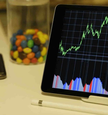 A tablet displaying stock market graphs next to a smartphone and a glass jar of colorful candies.