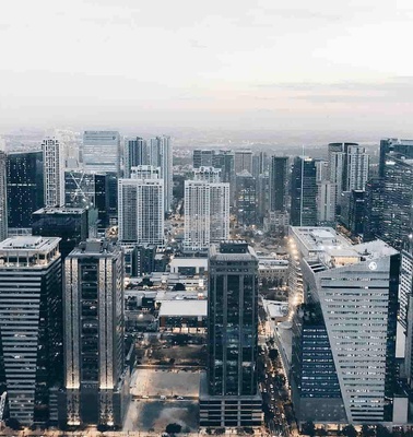 Aerial view of a dense modern cityscape with numerous skyscrapers and a hazy sky in the background.